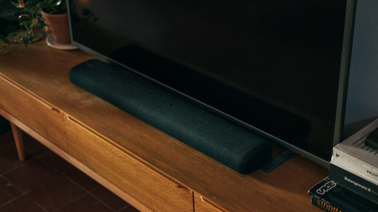 A slim soundbar sitting in front of a TV on a wooden console
